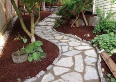 A curved stone walkway next to red mulch and shade plants.