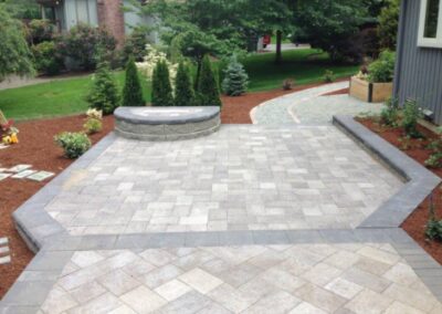 A grey custom designed patio next to walkway and mulched landscaped area.