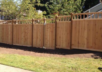 A staggered wood fence with wood caps along mulch and lawn area.