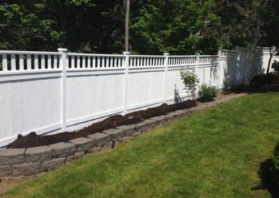 White straight fence with white caps and landscaping with lawn and mulch.