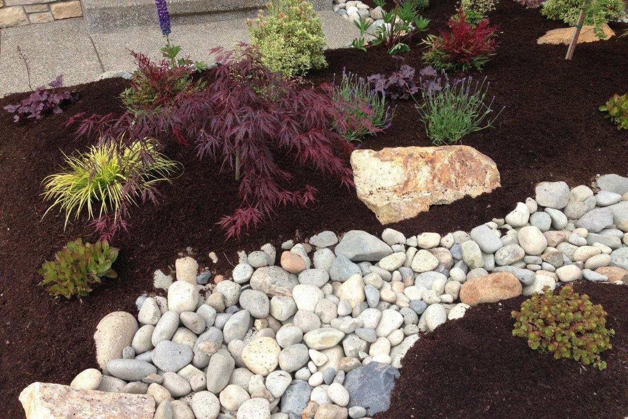 Image of a rock bed running through a planting bed, used for drainage control services.